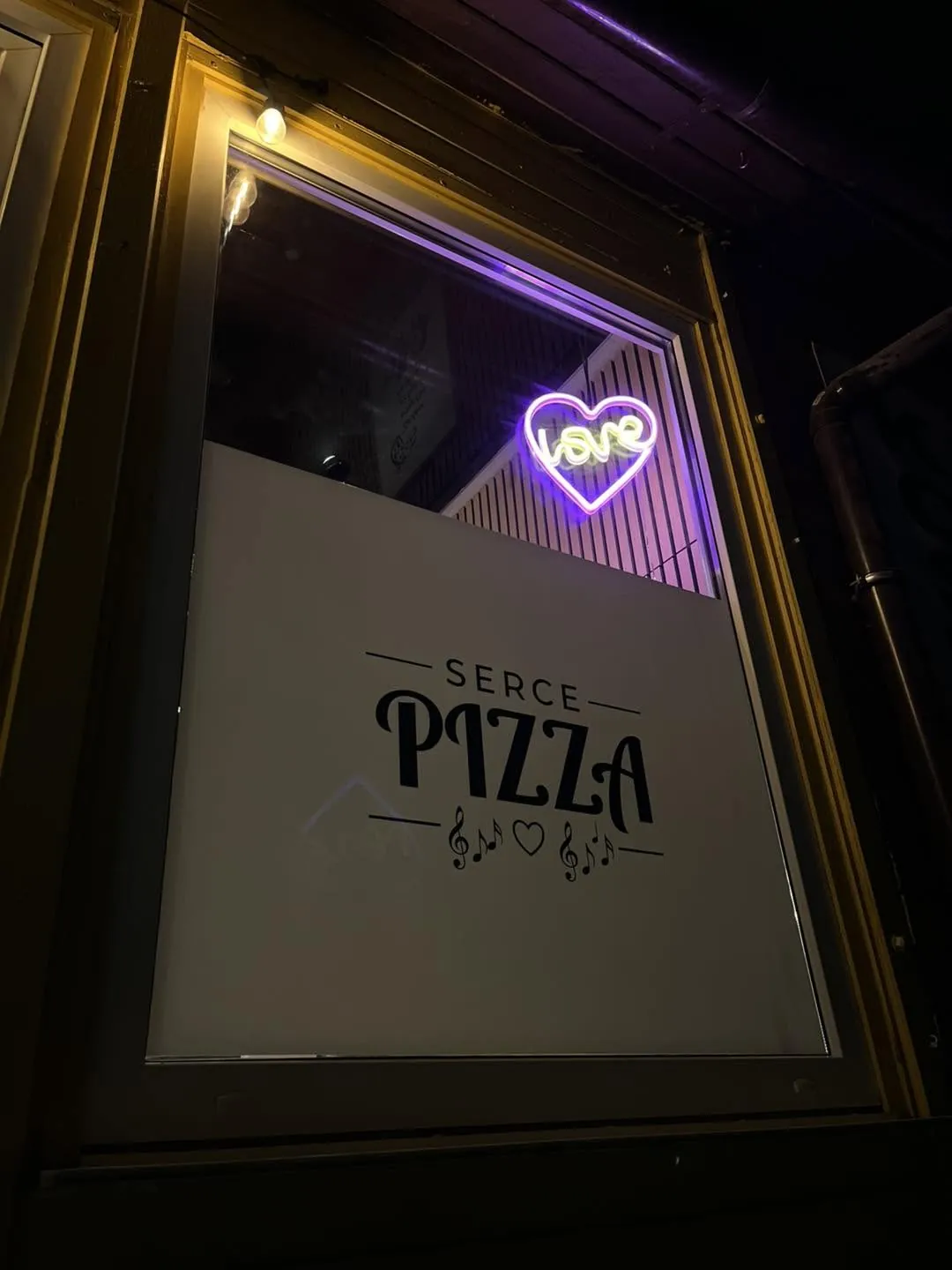 Wejście do Serce Pizza wieczorem, logo na szybie i fioletowy neon w kształcie serca