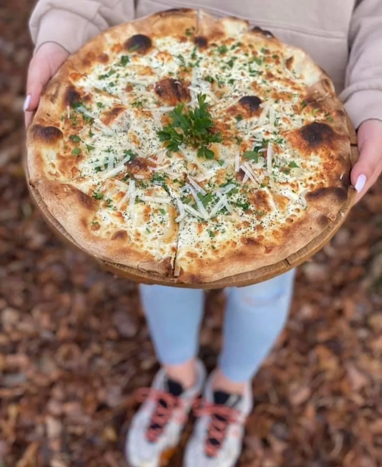 Biała pizza z ziołami na drewnianej desce, pod nogami jesienne liście