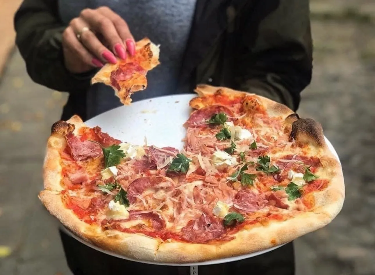 Dłoń sięga po kawałek pizzy z szynką