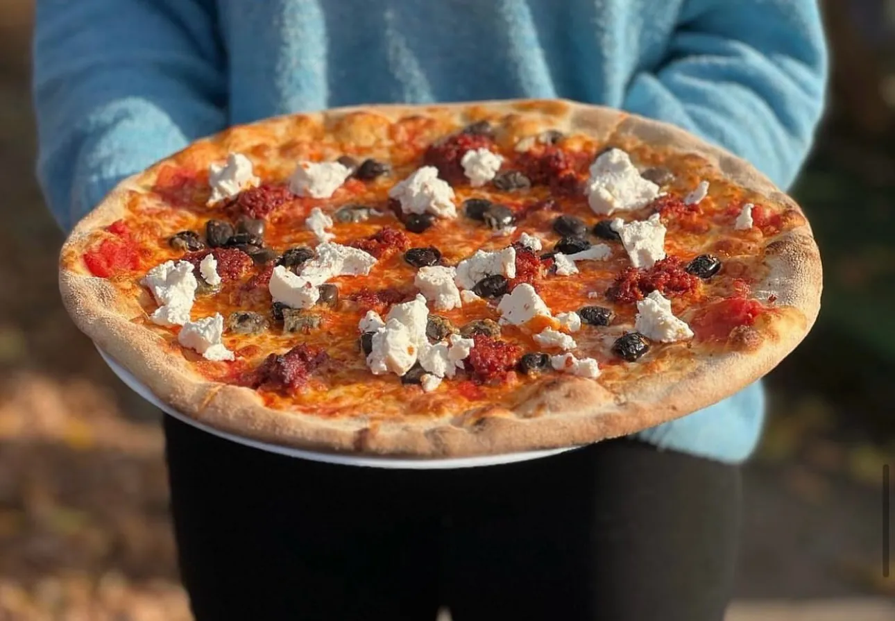 Pizza z oliwkami i białym serem trzymana nad stołem